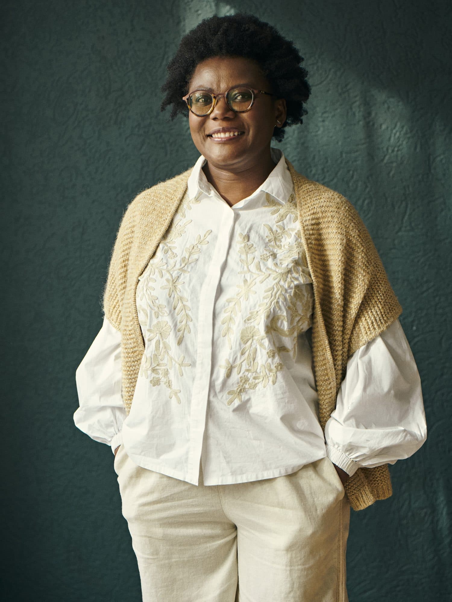Alberta Opoku in een witte geborduurde blouse voor een donkergroene muur